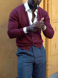 Stylish man wearing a burgundy V-neck button-front knit cardigan with gray trousers.